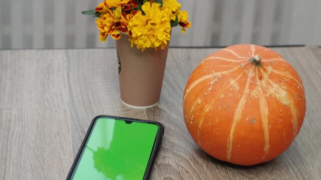 Autumn Thanksgiving arrangement, still-life, smartphon. Harvested pumpkins, a beautiful bouquet of yellow and orange flowers, fruits and vegetables, autumn leaves, and red berries on a wooden table. A