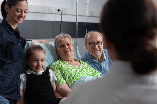 Oxygen, family and communication around senior patient using nasal cannula as clinician discusses care with child and relatives near bed for treatment planning, recovery support and guidance.