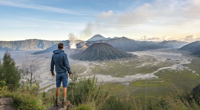 Young man in front of volcanic landscape, view in Tengger Caldera, smoking volcano Gunung Bromo, in front Mt. Batok, behind Mt. Kursi, Mt. Gunung Semeru, National Park Bromo-Tengger-Semeru, Java, Indonesia