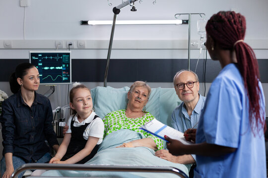 Oxygen, family and consultation around senior patient using nasal cannula as nurse reviews care with child and adult relatives at hospital bedside for recovery planning, communication and reassurance.