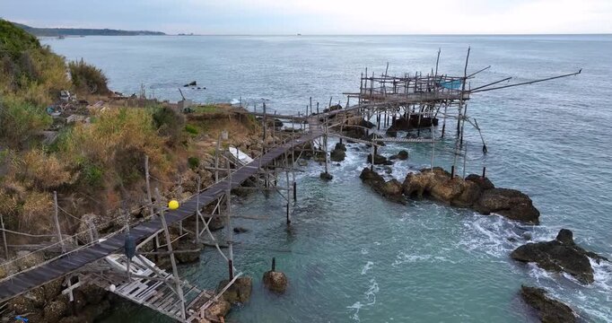 Aerial view of Trabocco Lupone, a traditional wooden fishing structure extending over the Adriatic Sea with rocky coastline in Marina di San Vito, Provincia di Chieti, Italy.