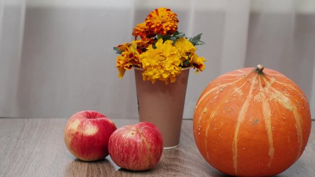 Autumn Thanksgiving arrangement, still-life background. Harvested pumpkins, a beautiful bouquet of yellow and orange flowers, fruits and vegetables, autumn leaves, and red berries on a wooden table. A