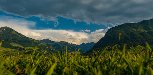 Fototapeta premium Mountain rests beneath large white clouds. Mountain contrasts with a clear blue sky. Dramatic cloudscape surrounds mountain above the valley. Bright cumulus clouds gather behind mountain.