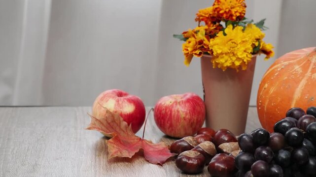 Autumn Thanksgiving arrangement, still-life background. Harvested pumpkins, a beautiful bouquet of yellow and orange flowers, fruits and vegetables, autumn leaves, and red berries on a wooden table. A