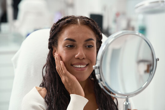 Cosmetic dentistry smile makeover concept focused on tooth color and front teeth appearance. African woman smiles broadly, showing bright teeth with her hand against her cheek.