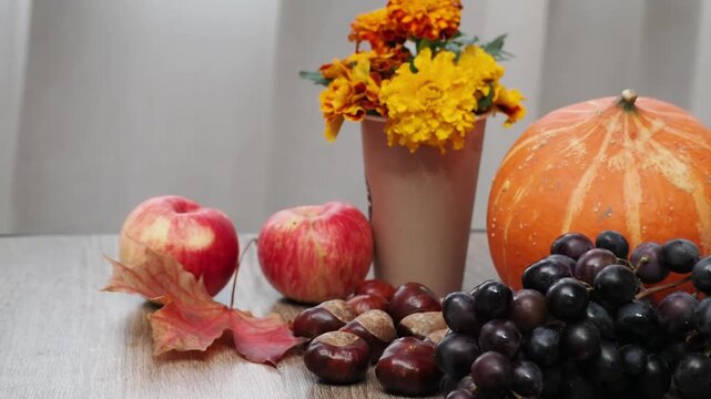 Autumn Thanksgiving arrangement, still-life background. Harvested pumpkins, a beautiful bouquet of yellow and orange flowers, fruits and vegetables, autumn leaves, and red berries on a wooden table. A