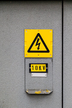 A high-voltage warning sign is mounted on a textured gray wall indicating a 10 kilovolt electrical hazard.