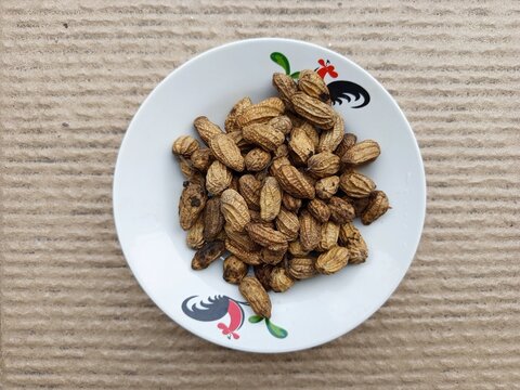Boiled peanuts served in a traditional rooster ceramic plate on a brown textured background. 