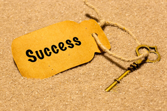 Old vintage key in sand with a card label with the word success. Phrase 'key to success' concept