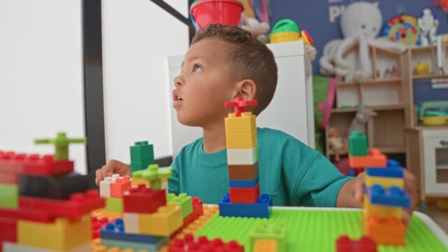 Boy using hands to stack colorful blocks on a play table inside a building; concentration creativity imagination.