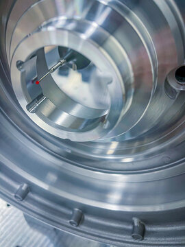 Close up view of CMM measurement probe with red ruby tip checking dimensions and tolerances inside a high precision machined metallic mechanical part in quality control laboratory