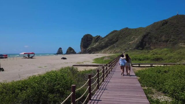 Tracking shot of two female friends walking with their arms around each other along the new beach trail leading to the San Lorenzo lighthouse, located on the cliffs of Manta, Ecuador.