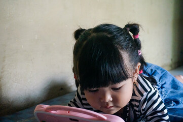 Cute little Asian girl playing with a smartphone or tablet device at home. © Rendi