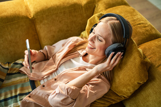 Smiling woman with headphones streaming music on smartphone at home