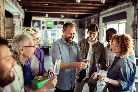 Coworkers celebrating as man opens champagne in office