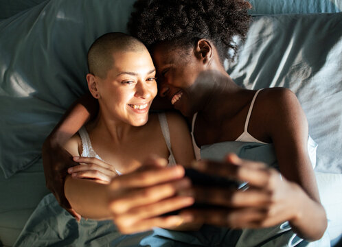 Smiling couple taking selfie while cuddling in bed