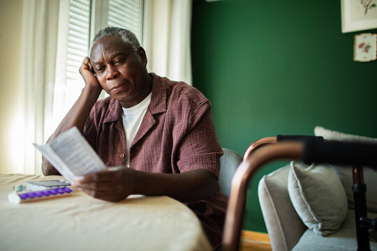 Senior man reading medication instructions at home with walker nearby