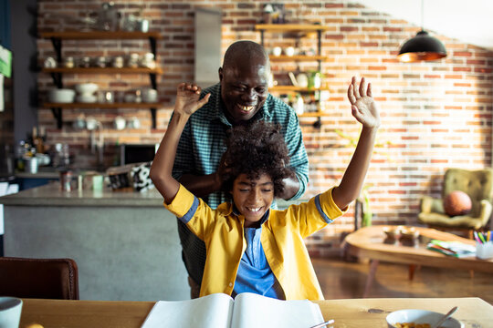 Man cheers as boy celebrates homework at kitchen table
