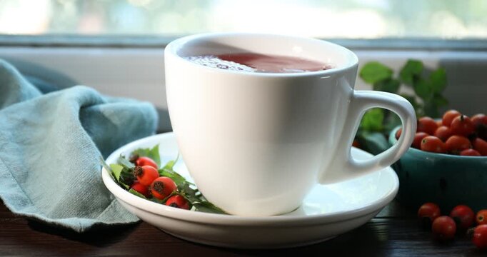 Pouring rosehip tea into cup on window sill indoors, closeup