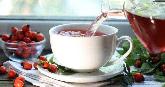 Pouring rosehip tea into cup on window sill indoors, closeup