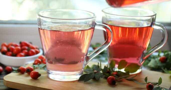 Pouring rosehip tea into cup on window sill indoors, closeup