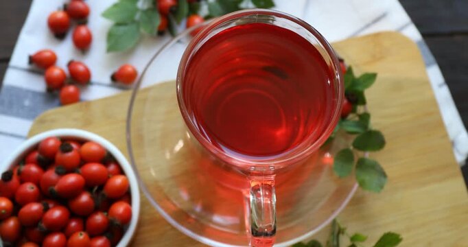 Rosehip tea in cup and berries with leaves on wooden table, above view