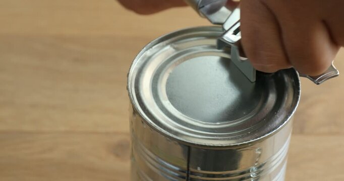 Woman opening tin of pickled pineapple rings with can opener at wooden table, closeup