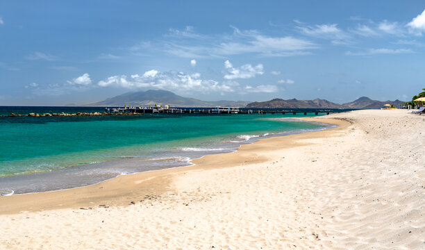 Scenic view of sandy Pinneys Beach with turquoise sea water, pier, and Saint Kitts in the distance on the island of Nevis.