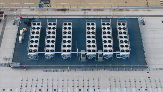Aerial view of HVAC ventilation and cooling fans arranged in rows on a flat industrial rooftop, featuring metallic structures and circular fan units, Peterborough, England, United Kingdom.
