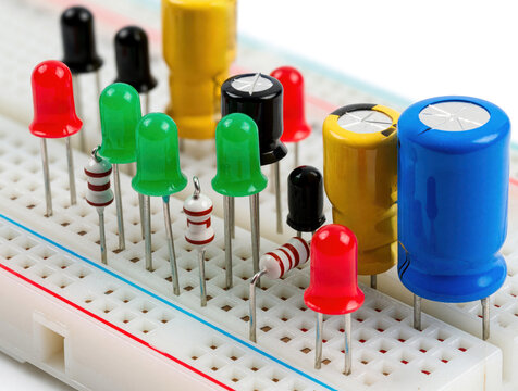 Close up of electronic parts on white breadboard. Resistors, colorful LED lights, electrolytic capacitors connected for circuit prototype. Engineering student hobbyist builds electrical hardware
