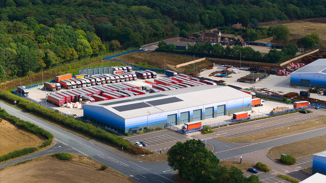 Aerial view of industrial logistics warehouses with rows of parked HGVs and trailers at a distribution center in Bury St Edmunds, England, United Kingdom.