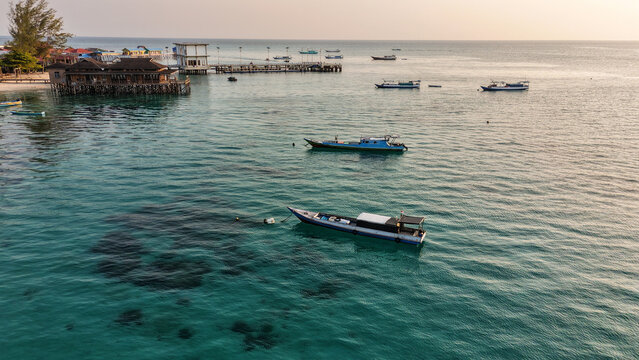 Aerial view of Local Fisherman Boat Derawan featuring turquoise waters, coral reefs, and wooden stilt houses surrounded by lush tropical vegetation, Berau, East Kalimantan, Indonesia.