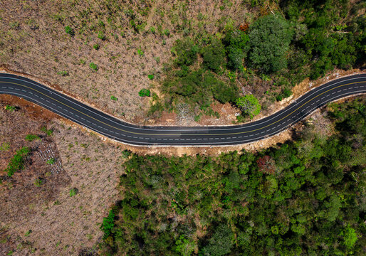 Aerial view of a newly paved winding asphalt road snaking through dry, deciduous hills during the dry season to JLS or South Malang beaches in Malang, East Java, Indonesia.