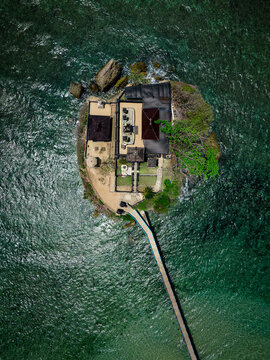 Aerial view of the Balekambang Beach temple on a rocky islet, connected by a long bridge, surrounded by clear turquoise sea water, Malang, East Java, Indonesia.