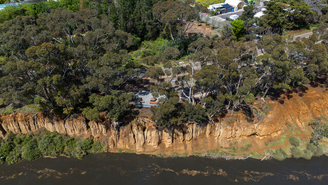 Aerial drone view of the K Road Cliffs at Werribee South, Melbourne, Victoria, Australia, with a tall eroded orange cliff face above water of the Werribee River, eucalyptus trees along the cliff.