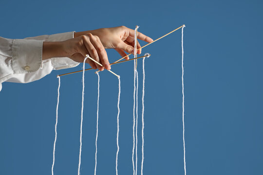 Manipulation and control concept, hands operating a marionette crossbar with strings to influence behavior and corporate power dynamics on blue background