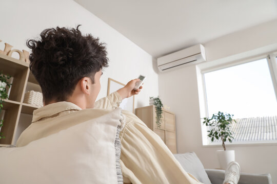 Climate control and energy efficiency, man using remote to adjust air conditioning temperature in a comfortable living room during a hot summer day
