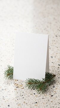 Blank folded greeting card mockup with pine tree branches and paper clip on a terrazzo surface for Christmas and winter design