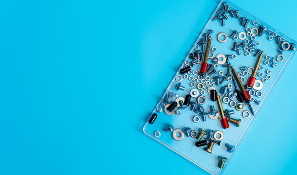 Top view of metal bolts, nuts, washers and screws arranged in a clear plastic tray on blue background, mechanical fastener hardware for assembly, repair, construction and technician work