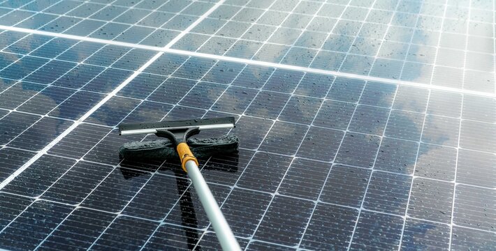 Cleaning wet solar panels with microfiber mop on rooftop photovoltaic system, maintenance service for efficient solar power generation, renewable energy and sustainable development technology