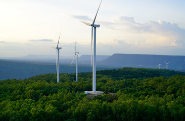 Fototapeta na wymiar Wind turbines generating renewable electricity across a green forest and mountain landscape at sunset. Sustainable energy, clean technology, low carbon development and environmental conservation.