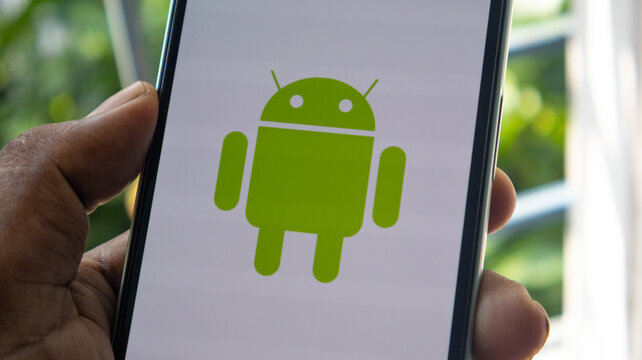 A hand holding a smartphone displaying the green android robot logo on a white screen representing mobile technology and operating systems.