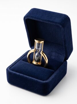 Golden ring with miniature hourglass instead of diamond in dark blue velvet jewelry box, timeless love or waiting concept