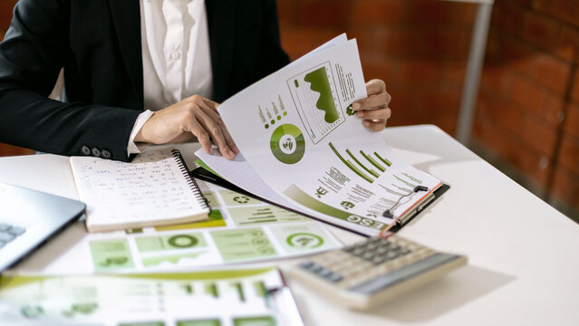 Woman reviewing ESG sustainability report with environmental data charts and business documents for corporate strategy and planning