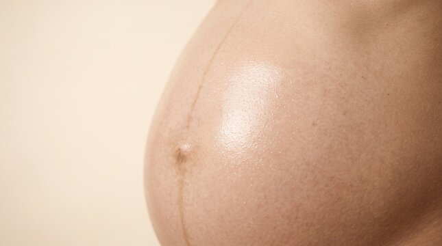 Macro close-up of pregnant woman bare belly showing linea nigra and glistening massage oil for stretch mark prevention