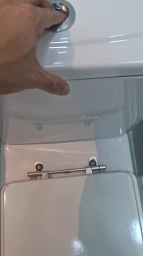 Close-up of a hand pressing a toilet flush button in a clean bathroom, illustrating everyday sanitation, bathroom hygiene and a routine household task