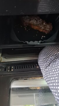 Home cook carefully removes a browned cut of beef from an open air fryer with a kitchen utensil, documenting a practical stage of everyday meal preparation