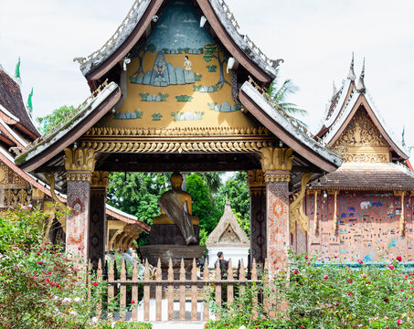 A view through an ornate gate at Wat Xiengthong reveals a golden Buddha statue within the temple grounds, surrounded by lush greenery and traditional Lao architecture.