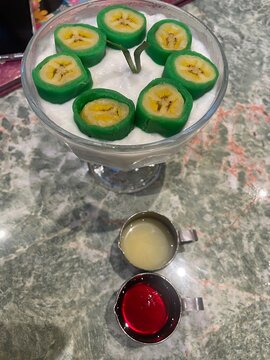 A Bowl of Es Pisang Ijo Makassar With Syrup and Ice.
Delicious Es Pisang Ijo in a bowl, authentic culinary from Makassar Indonesia. Green banana wrapped in pandan dough with pink syrup, vla sauce 