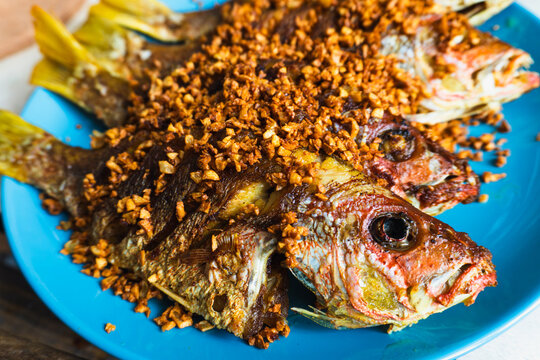 Close-up of deep-fried whole fish with turmeric and crispy garlic, served on a blue plate